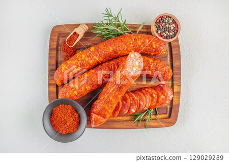 Spicy dry sausages and sliced salami served on a wooden board with paprika, peppercorns, and rosemary garnish 129029289