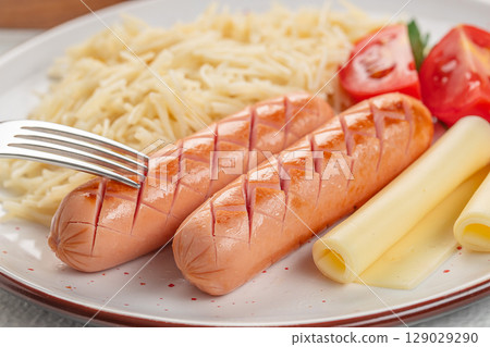 Grilled sausages served with grated pasta, rolled cheese slices, and fresh tomato quarters on a white plate Grilled sausages served with grated pasta, rolled cheese slices, and fresh tomato quarters on a white plate 129029290