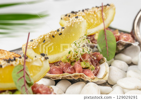 A gourmet seafood appetizer with diced tuna, avocado, lemon wedges topped with sesame seeds, and microgreens served on shells over white stones A gourmet seafood appetizer with diced tuna, avocado, lemon wedges topped with sesame seeds, and microgreens served on shells over white stones 129029291