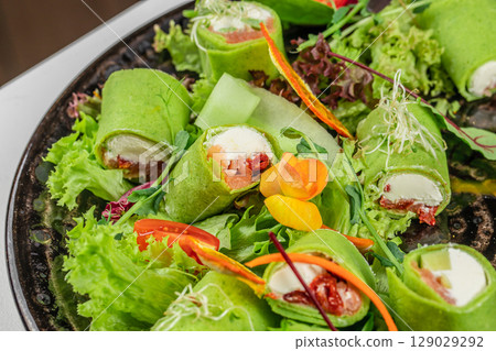 Colorful spinach wraps filled with cream cheese, smoked salmon, and sun-dried tomatoes, served on a fresh bed of assorted greens and edible flowers 129029292