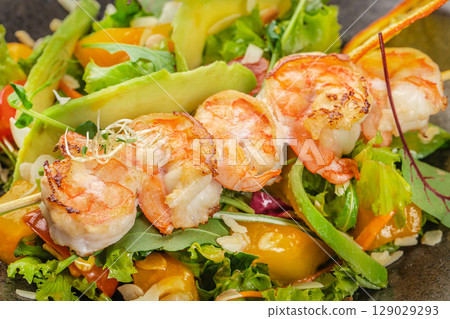 Grilled shrimp skewers rest atop a vibrant medley of fresh greens, ripe avocado, and colorful vegetables, creating a delicious and visually stunning seafood salad 129029293