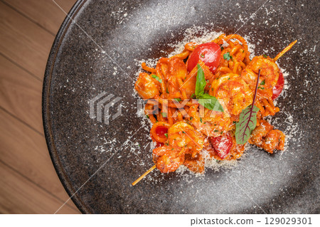Spaghetti with shrimp in vibrant tomato sauce is garnished with fresh herbs and grated cheese for a flavorful seafood pasta dish 129029301