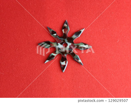 A star-shaped shuriken painted in military colors on a red background. The inscription on the shuriken reads Kohga Ninja. A star-shaped shuriken painted in military colors on a red background. The inscription on the shuriken reads Kohga Ninja. 129029507