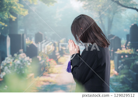 A woman wearing mourning clothes praying at a cemetery 129029512