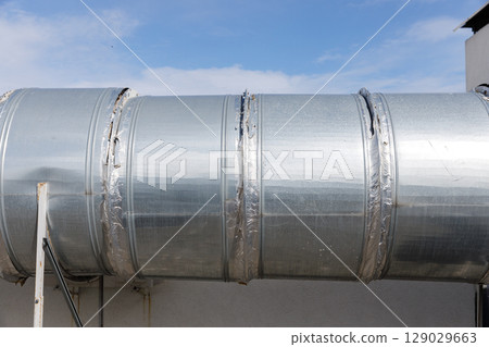 Shiny Metal Ducting Installed on the Exterior of a Building with Brilliant Blue Sky in the Background Providing a Modern Industrial Vibe and Strong Aesthetic Appeal 129029663