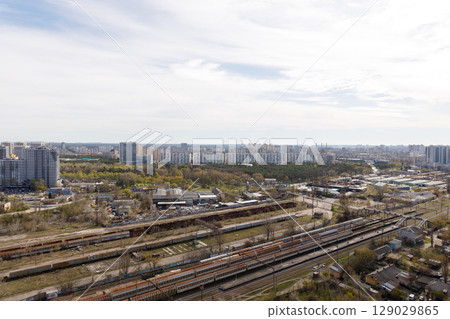 Aerial View of Urban Landscape Featuring Industrial Areas and Residential Buildings with Train Tracks in the Foreground Under a Partly Cloudy Sky and Lush Green Surroundings 129029865