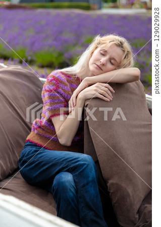 A Serene Moment: A Young Woman with Blonde Hair Relaxing on a Sofa in a Lavender Field, Capturing Tranquility and Comfort in a Beautiful Nature Setting 129029928