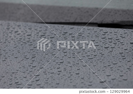 Close-up View of Raindrops on a Car Surface Captured in Natural Light, Showcasing the Beauty of Rain and Water Drops on Smooth Black Paintwork 129029964