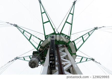 An Impressive Structure: A View from Below of a Tower with Green Support Beams and Mechanical Components Against an Overcast Sky 129029993