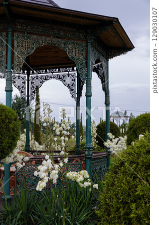 Elegantly Crafted Gazebo Surrounded by Beautiful Blossoms in a Lush Garden Setting with Verdant Greenery and Charming Atmosphere for Relaxation and Enjoyment of Nature's Splendor 129030107