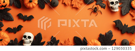 Halloween themed background with copy space and frame of spooky decorations including pumpkins, skulls, bats, and leaves on orange backdrop 129030335