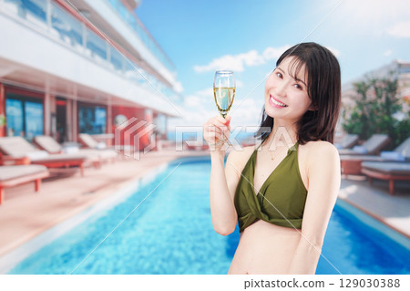 Young woman wearing swimsuit drinking sparkling wine by resort pool 129030388