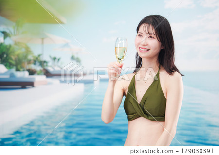 身穿泳衣的年輕女子在度假村泳池畔喝氣泡酒 129030391