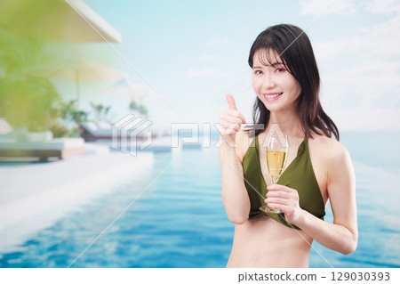 身穿泳衣的年輕女子在度假村泳池畔喝氣泡酒 129030393