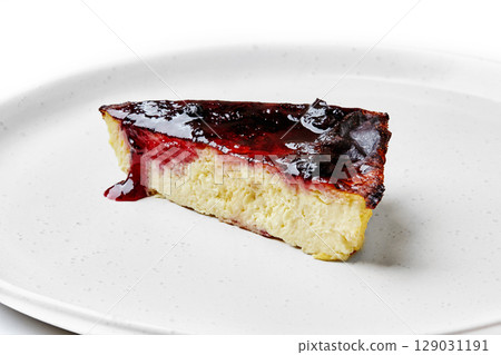 Slice of cheesecake with blueberry sauce dripping onto white plate 129031191