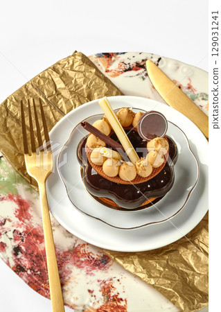 Delicious chocolate and caramel tart served on elegant plate with golden cutlery 129031241