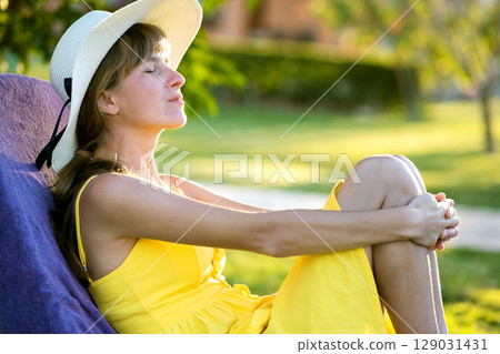 Young woman relaxing outdoors on sunny summer day. Happy lady lying down on comfortable beach chair daydreaming thinking. Calm beautiful smiling girl enjoying fresh air relaxing with closed eyes. Young woman relaxing outdoors on sunny summer day. Happy lady lying down on comfortable beach chair daydreaming thinking. Calm beautiful smiling girl enjoying fresh air relaxing with closed eyes. 129031431