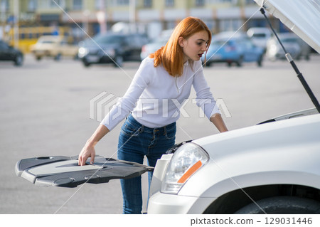 Young stressed woman driver standing near broked car with open hood. Young stressed woman driver standing near broked car with open hood. 129031446