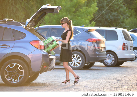 Young female driver loading luggage suitcase bag inside her car. Travelling and vacations concept 129031469