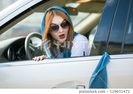 Young fashionable woman driver has her scarf jammed in vehicle doors and is pulling it out. Young fashionable woman driver has her scarf jammed in vehicle doors and is pulling it out. 129031472