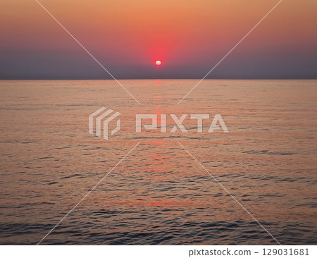 Captivating sunrise over the calm sea. Peaceful seascape at dawn with soft gradients of orange and pink on the sky reflecting on the water 129031681