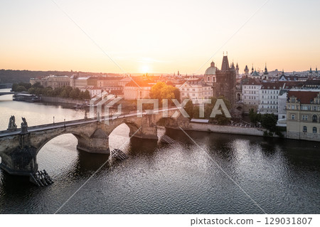 A breathtaking sunrise casts warm light over the historic Charles Bridge in Prague, illuminating the Vltava River and the charming old town buildings on the banks. 129031807