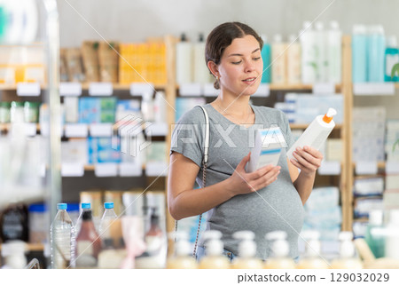 Pregnant woman customer holding and selecting cream or skin care product in drugstore 129032029