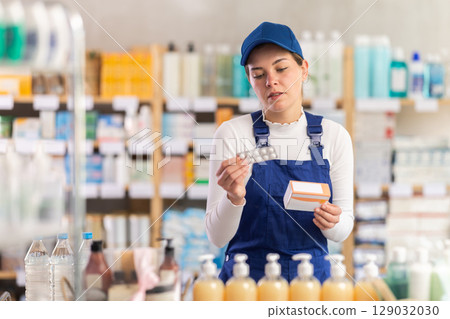 In sales area of pharmacy, builder woman examines packaging of tablet pill 129032030