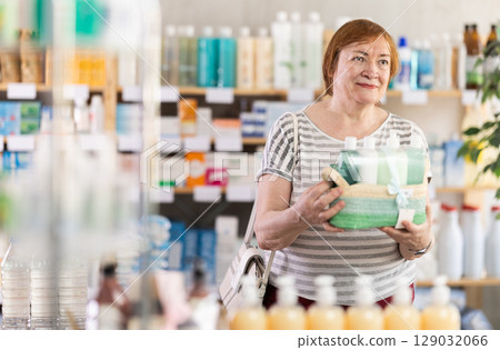 Mature woman chooses gift consisting of various shampoos, creams and other cosmetics for body care 129032066