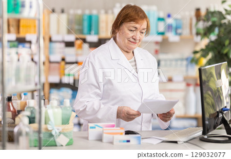 Professional elderly female pharmacist searches for information about medicines on Internet 129032077