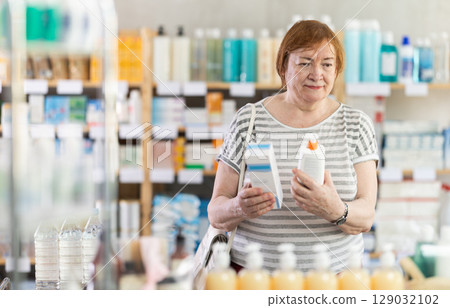 In sales area of pharmacy, mature woman examines packaging of cream 129032102