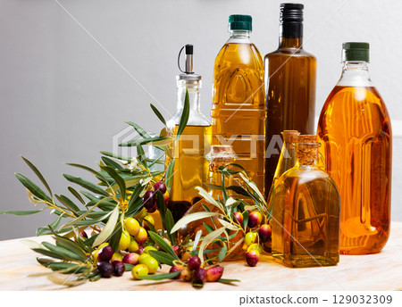 Glass bottles and carafes with fresh olive oil on wooden table with olive branches and fresh olives 129032309