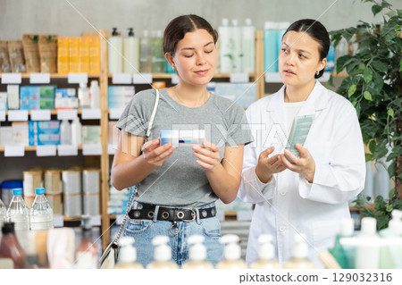 Attentive young girl buyer choosing medical ointment and professional asian female parmacist helping in pharmacy 129032316