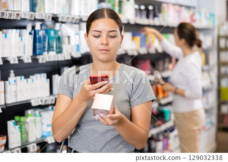 Woman customer using phone to search information about selected product at pharmacy Woman customer using phone to search information about selected product at pharmacy 129032338