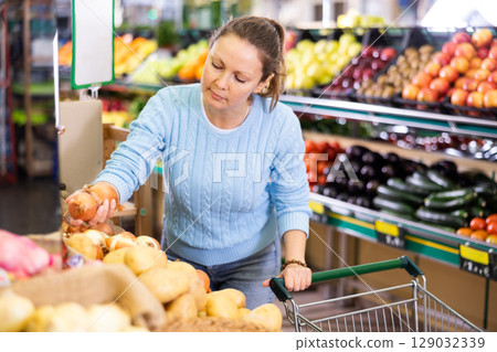 Positive middle-aged female buyer choosing onion in supermarket 129032339