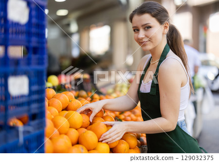 Working in supermarket - female salesman sorts through ripe tangerines on display case Working in supermarket - female salesman sorts through ripe tangerines on display case 129032375
