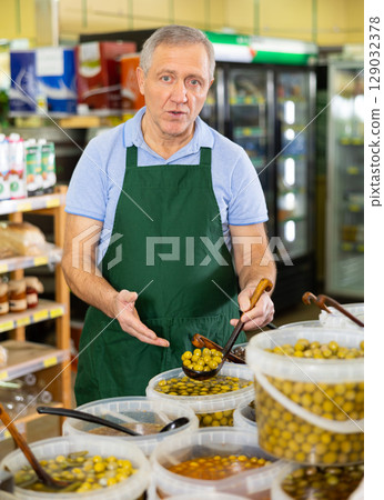 Elderly salesman showing olives in grocery store Elderly salesman showing olives in grocery store 129032378