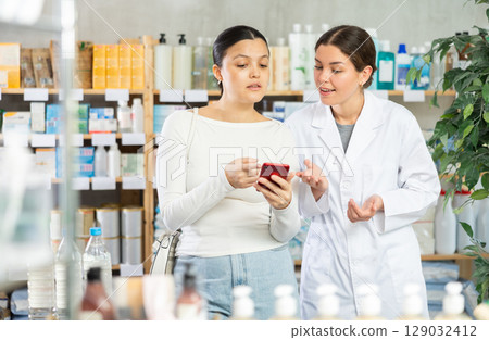 Woman showing prescription on phone to pharmacist at pharmacy 129032412