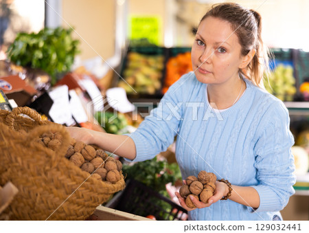 Portrait of busy middle-aged European woman buying walnuts in shell in grocery store 129032441