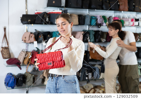 Girl stopped near accessories showcase, holds lady handbag in hands and examines product Girl stopped near accessories showcase, holds lady handbag in hands and examines product 129032509