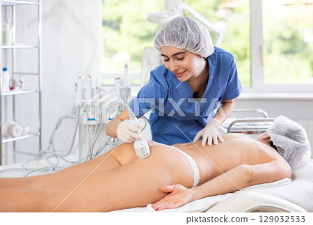 Female cosmetologist performing procedure using cooling attachment on woman client buttocks 129032533