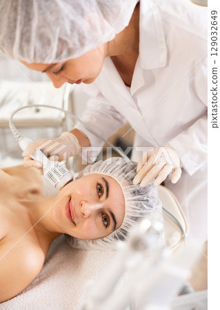 Young woman cosmetologist doing whitening procedure to young woman 129032649