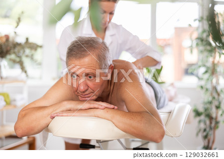 Relaxed old man having back massage therapy conducted by skilled masseuse Relaxed old man having back massage therapy conducted by skilled masseuse 129032661