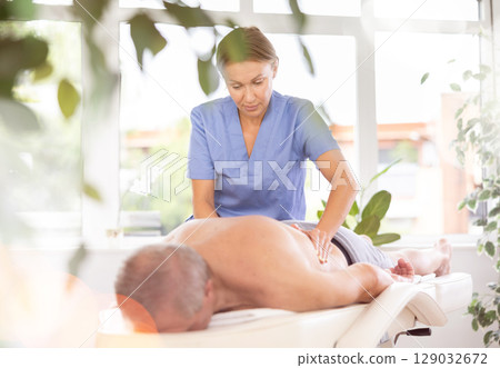 Skilled middle-aged masseuse conducting back massage for man client 129032672