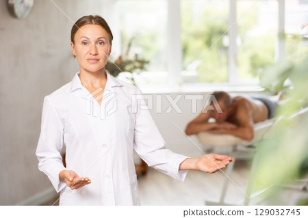 Positive middle-aged masseuse posing against background of therapy room Positive middle-aged masseuse posing against background of therapy room 129032745