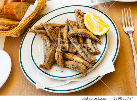 Tasty fried anchovies served with lemon at plate 129032784