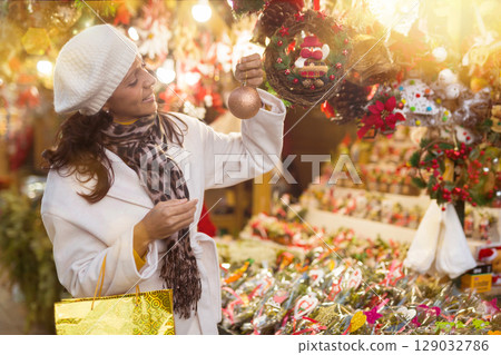 Hispanic woman choosing fir tree decorations at street Christmas fair 129032786