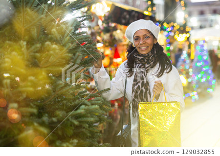 Cheerful hispanic woman looking for Christmas tree on outdoor market Cheerful hispanic woman looking for Christmas tree on outdoor market 129032855