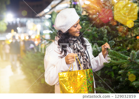 Smiling latin-american woman choosing fir tree for New Year celebration at street fair 129032859