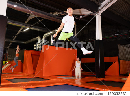 Emotional man jumping vertical and flying in trampoline sport center indoors Emotional man jumping vertical and flying in trampoline sport center indoors 129032881